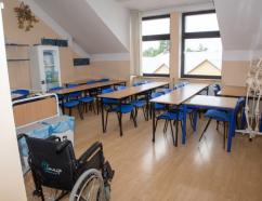 Sala opiekuna medycznego do wynajęcia w Zamościu, widok na stoły w układzie szkolnym oraz wózek inwalidzki 