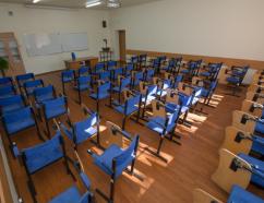Sala szkoleniowa, widok na krzesła z pulpitami, rzutnik oraz tablice suchościeralną