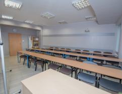 Sala konferencyjna, widok na krzesła tapicerowane z ławkami w układzie szkolnym, tablice suchościeralną oraz rzutnik