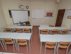 Sala szkoleniowa, widok na tablice multimedialną, tablice suchościeralną oraz krzesła z ławkami w układzie szkolnym