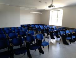 Sala szkoleniowa w budynku WSB przy al. Grunwaldzkiej w Gdańsku, widok na krzesła tapicerowane z pulpitami oraz flipchart i rzutnik multimedialny