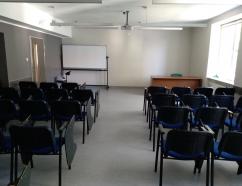 Sala szkoleniowa znajdująca się w budynku WSB w Gdańsku przy al. Grunwaldzkiej, widok na krzesła tapicerowane z pulpitami oraz rzutnik