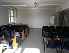 Sala szkoleniowa znajdująca się w budynku WSB w Gdańsku przy al. Grunwaldzkiej, widok na krzesła tapicerowane z pulpitami oraz rzutnik multimedialny