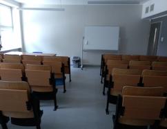 Sala szkoleniowa znajdująca się w budynku WSB w Gdańsku przy al. Grunwaldzkiej, widok na krzesła tapicerowane z pulpitami, biurko prowadzącego oraz rzutnik multimedialny