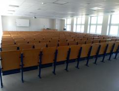 Aula znajdująca się w budynku WSB w Gdańsku przy al. Grunwaldzkiej, Sala szkoleniowa w budynku WSB przy al. Grunwaldzkiej w Gdańsku, widok na krzesła tapicerowane z pulpitami oraz rzutnik multimedialny widok na krzesła tapicerowane z pulpitami